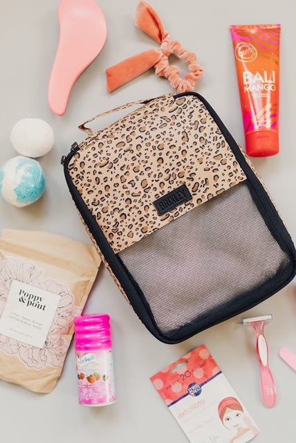Cheetah print (wild thing) small Brixley Bags packing cube displayed with various toiletry and bath products consisting of Bali Mango body lotion, a razor, women's shave gel, a face mask, Poppy & Pout product, bath bombs, and peach-colored hair tie.