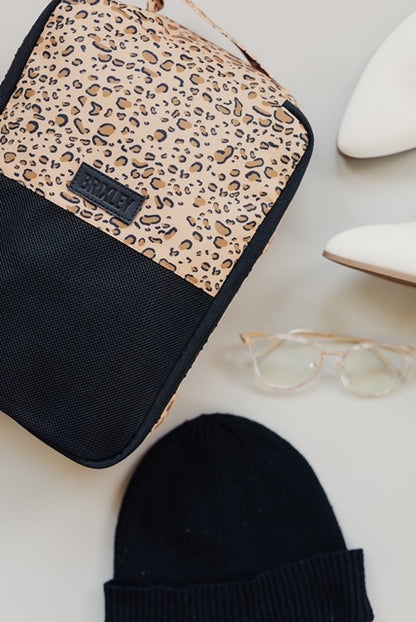 Cheetah print (wild thing) small Brixley Bags packing cube displayed with a pair of eyeglasses, a black beanie, and white women's shoes